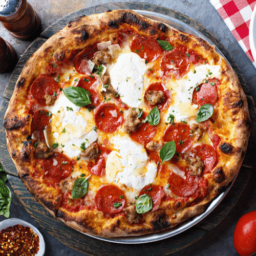 Close-up of a pepperoni and sausage pizza with fresh basil and melted cheese on a wooden table.